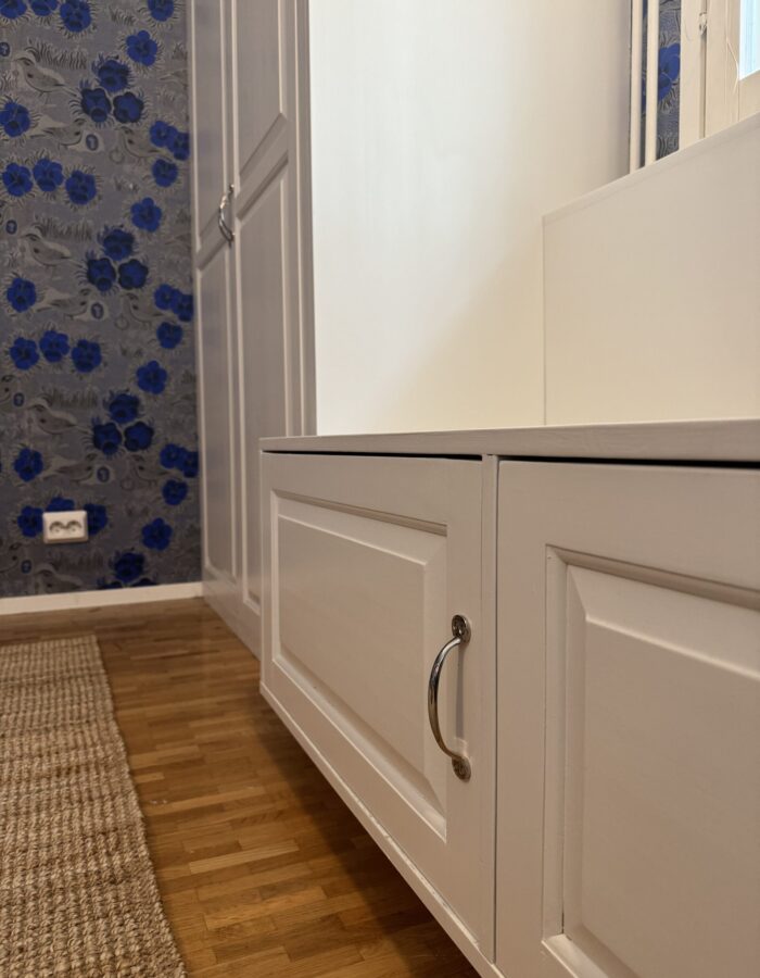 Valkoinen kiintokaluste ikkunan edessä asunnossa Järvenpäässä. Takana näkyy värikäs tapetti.